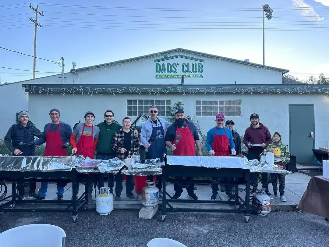 Dads in red aprons in front of the Dads' Club building
