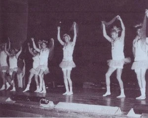 Black and white photo of dads dancing in tutus on stage